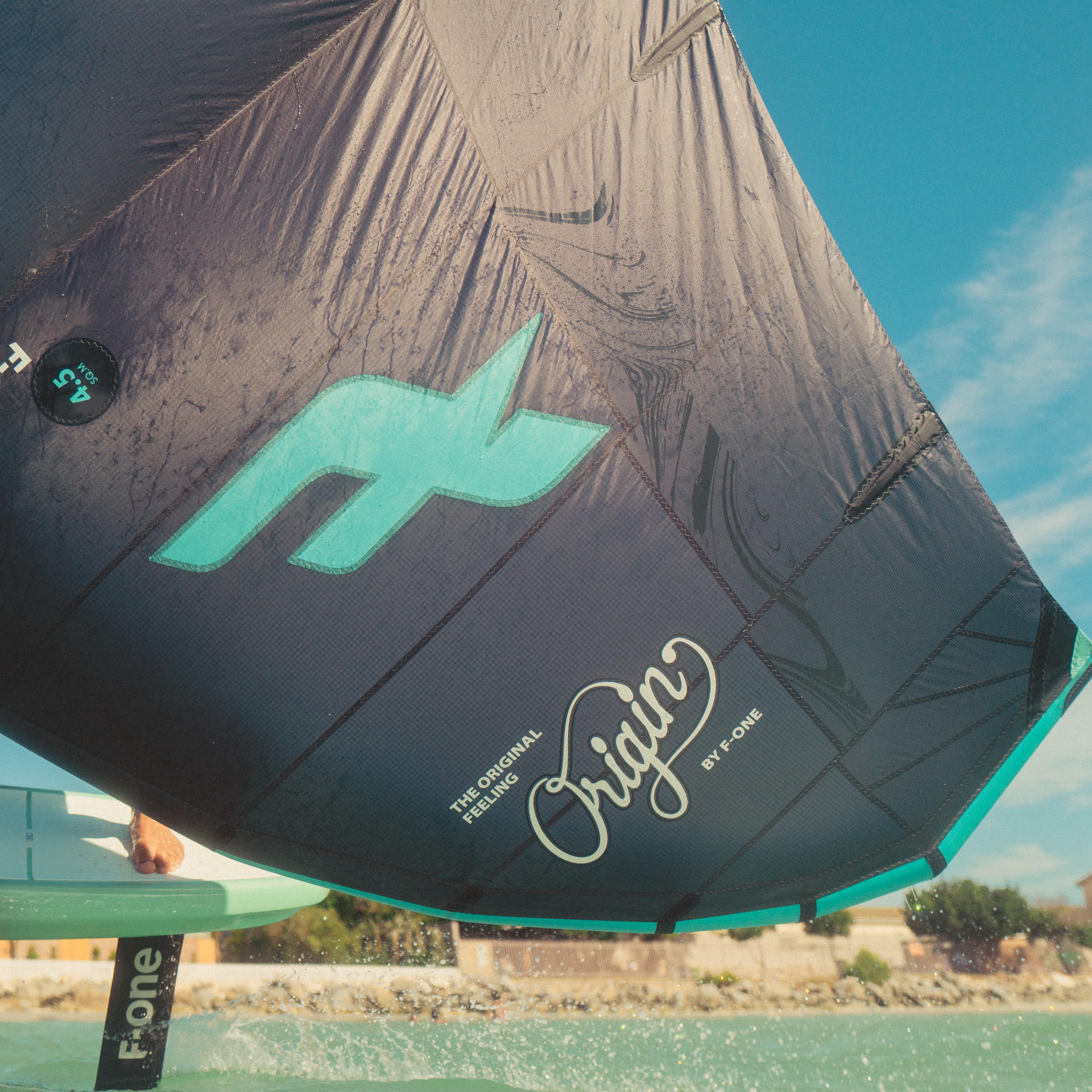 Gros plan sur l'aile F-One Origin utilisée par un rider en wingfoil, à peine visible derrière la wing.