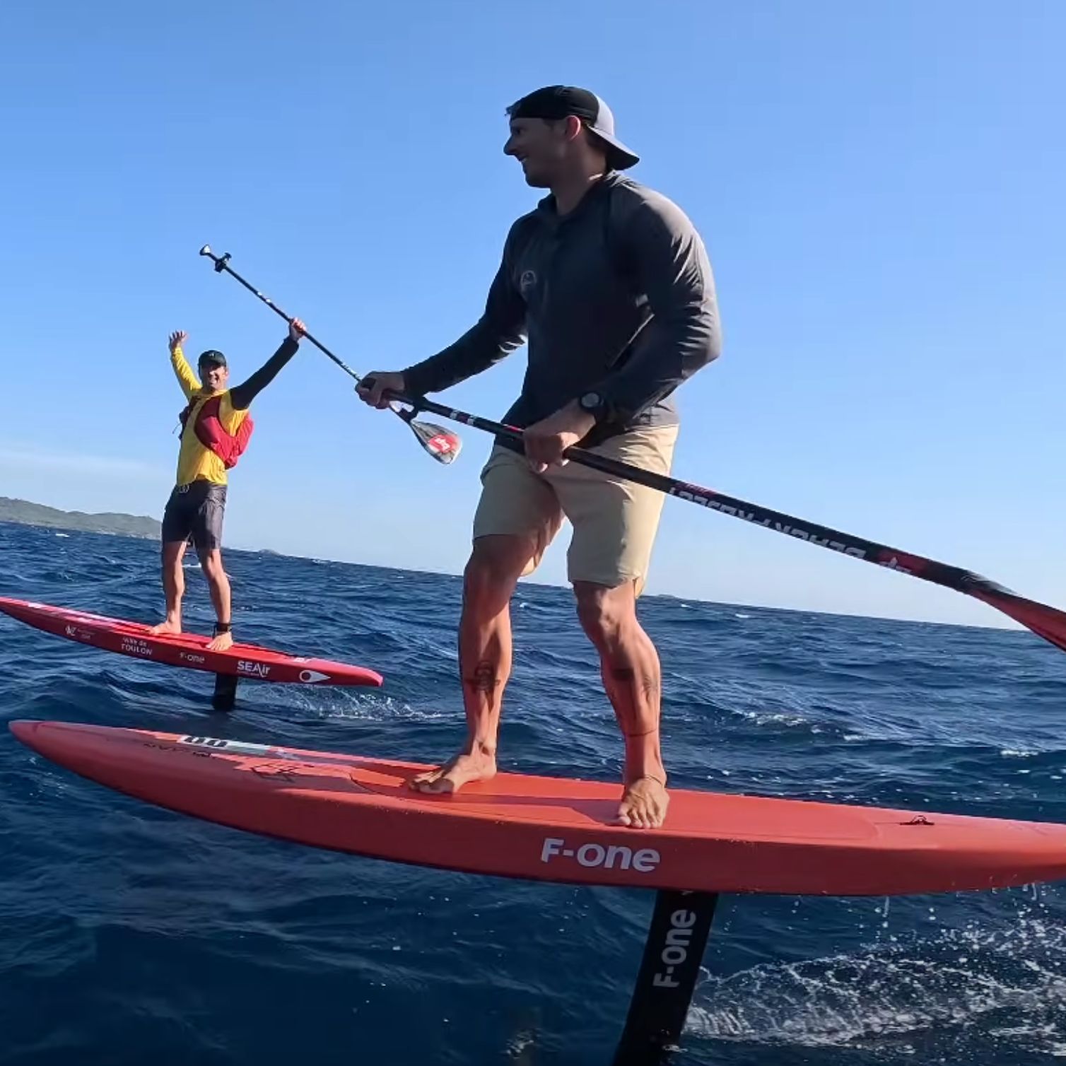Deux riders en SUP foil F-One naviguant en downwind, pagaie &agrave; la main, sur mer bleue avec du vent