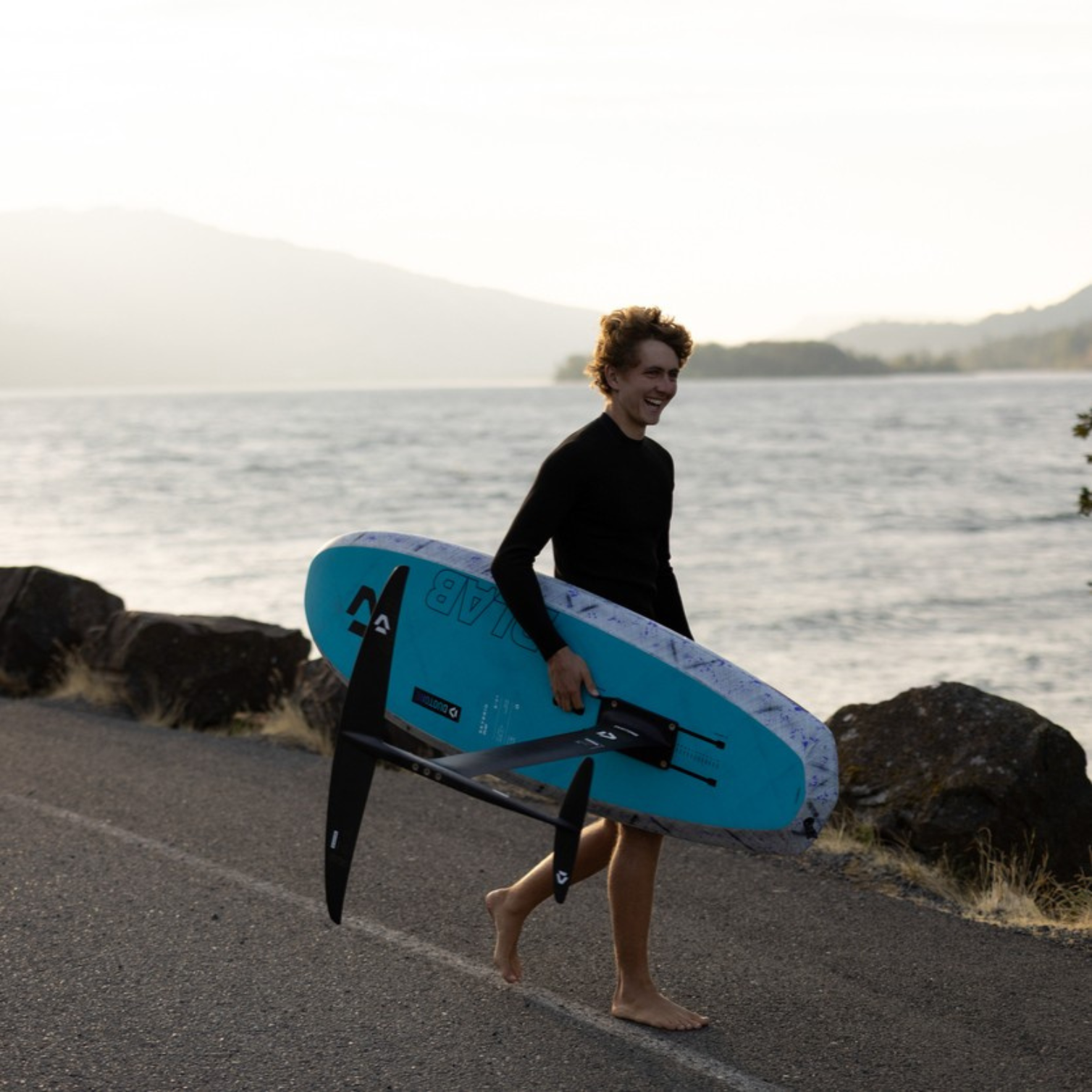 Rider portant sa planche de foil Duotone Crest D-LAB sur la plage au coucher de soleil